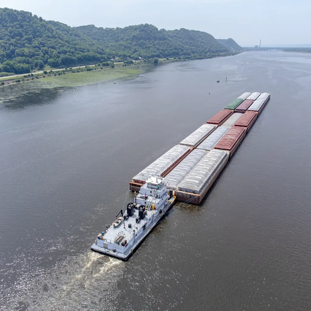 A towboat pushing a long connected group of covered cargo barges on a river.