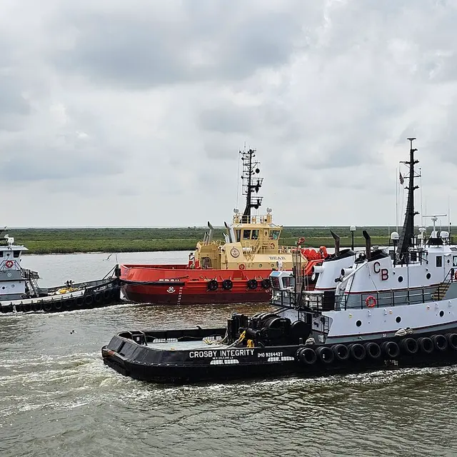 Two tugboats assisting a larger vessel in a harbor.