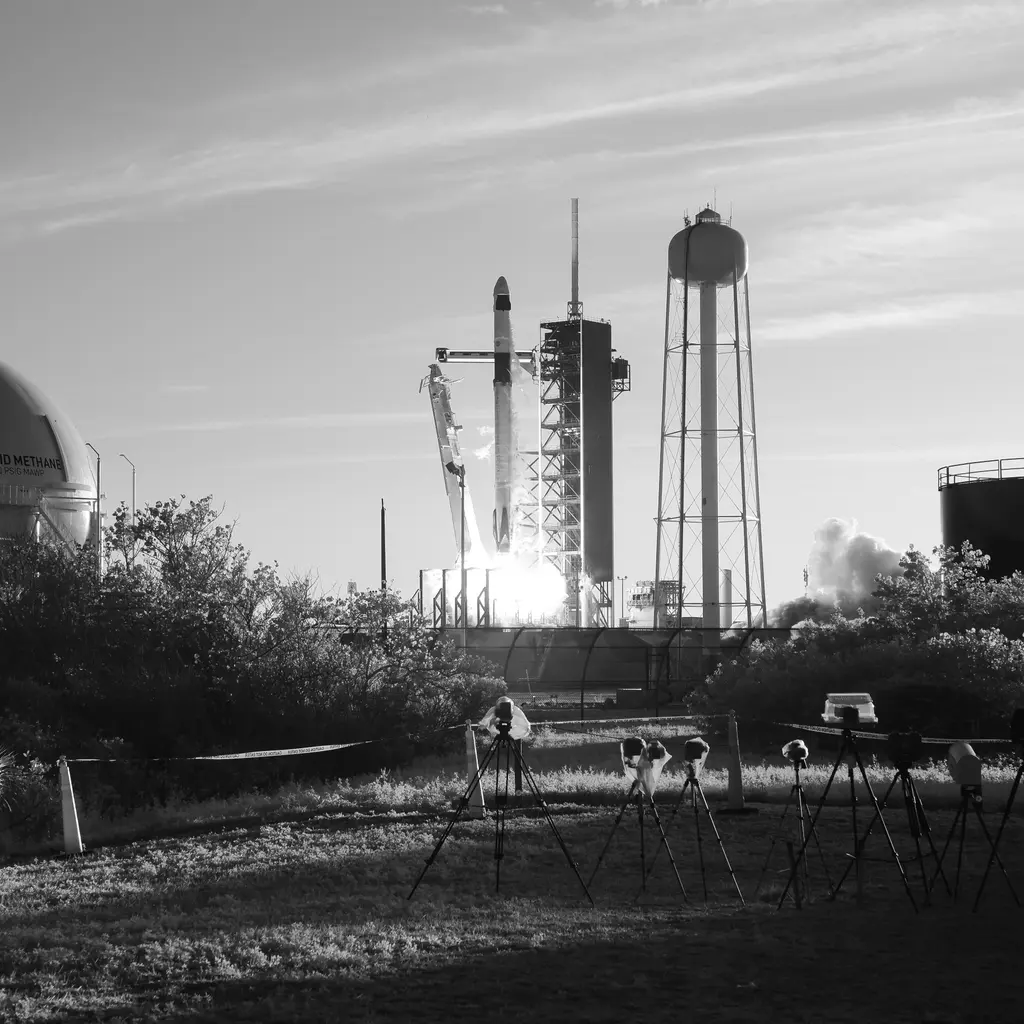 A rocket lifting off beside its launch tower in a black-and-white photograph.