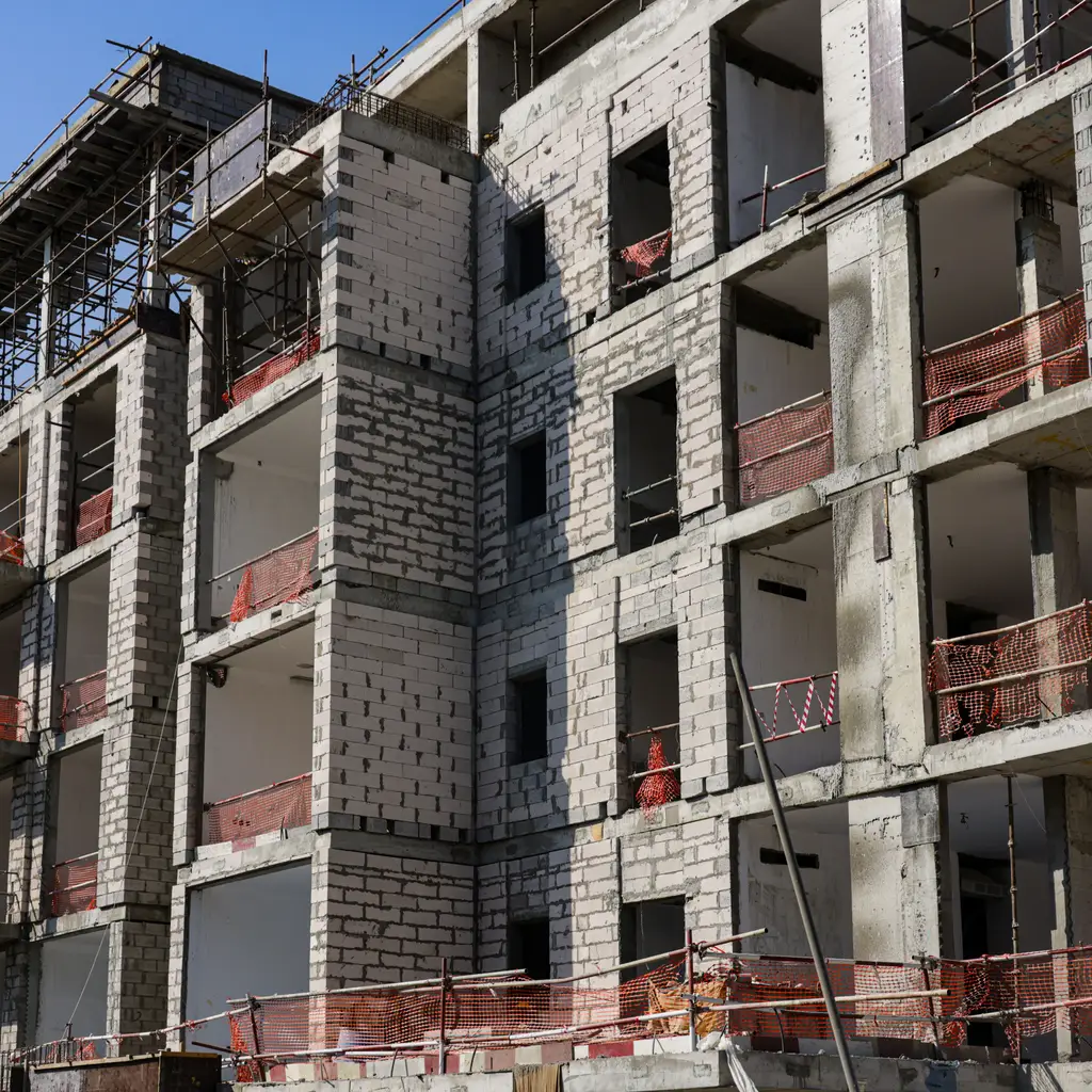 Multi-story apartment block under construction has open window bays, scaffolding and safety netting.