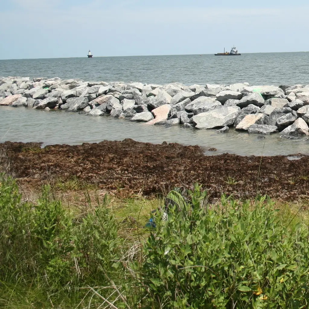 An armor-rock breakwater separates open coastal water from a sheltered strip beside the shoreline.