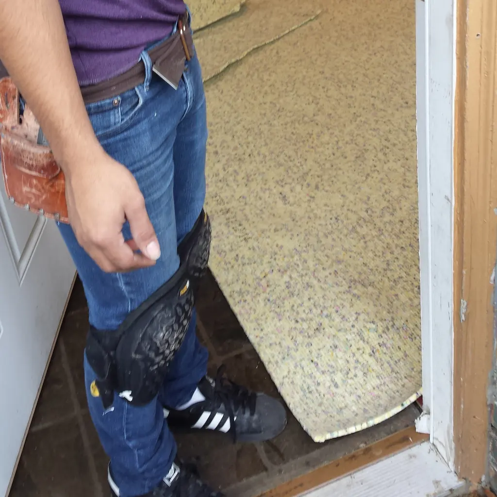 An installer wearing knee pads beside carpet underlay being fitted across a doorway.