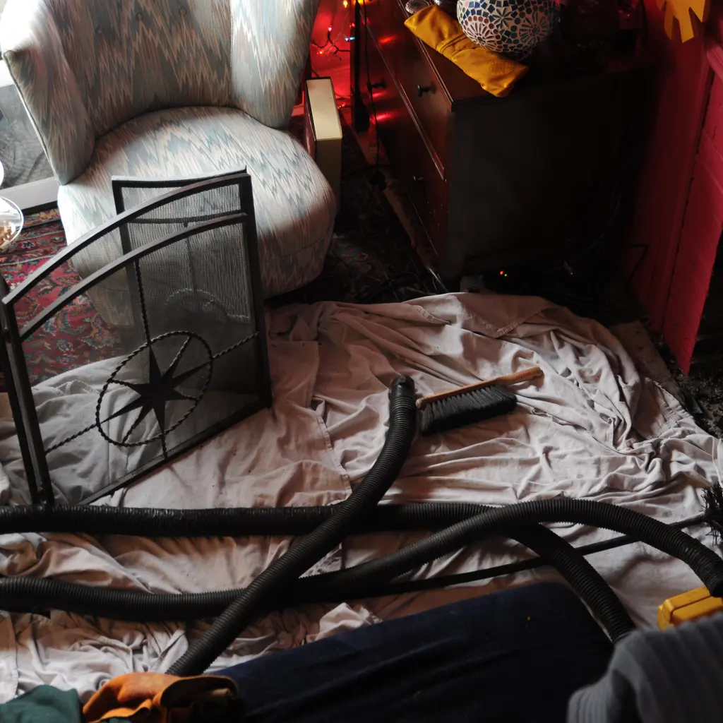 Chimney-cleaning hoses and tools rest on a protective floor cloth beside an open fireplace.