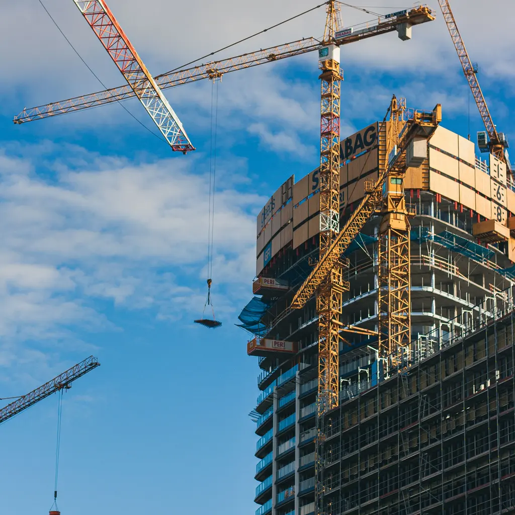 Tower cranes rise above a high-rise office building with exposed structure and facade works.
