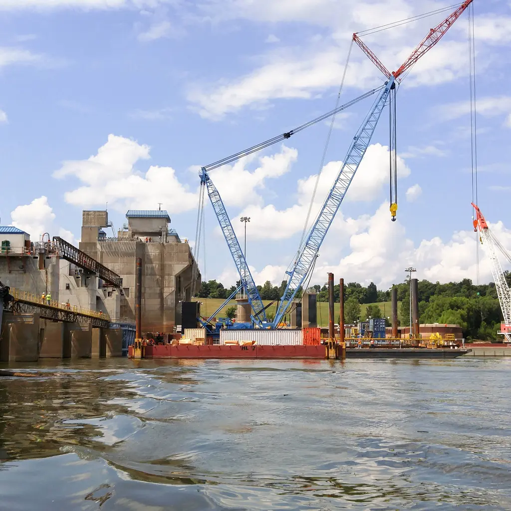 Cranes and work barges beside a concrete dam construction site.