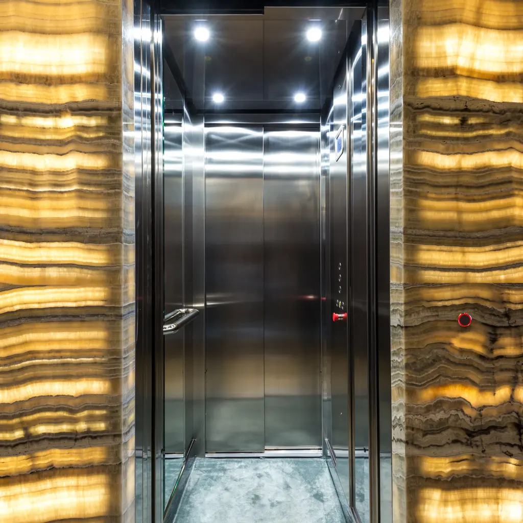 An empty stainless steel elevator cabin with open doors, control buttons and illuminated interior finishes.