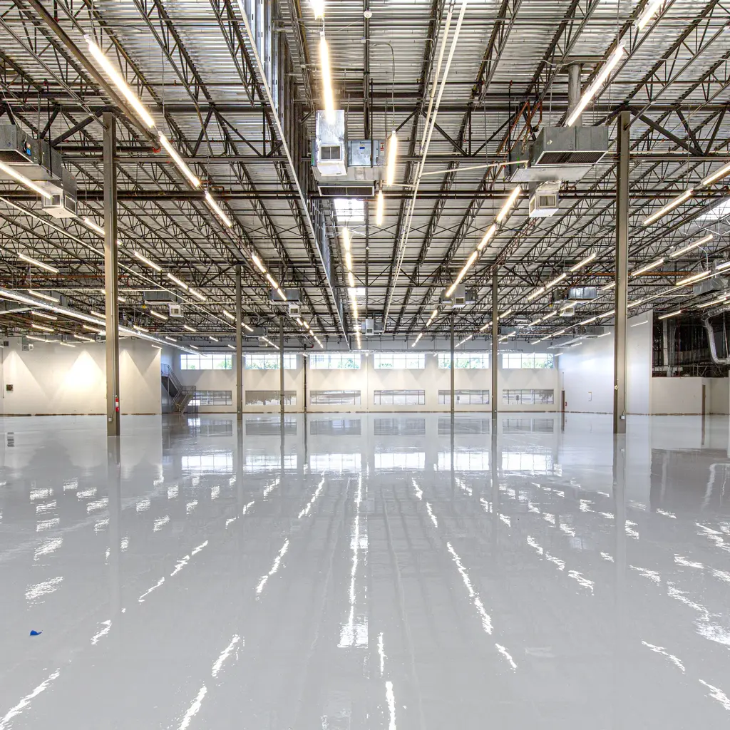 A large industrial interior with a seamless glossy epoxy floor reflecting the overhead structure and lights.