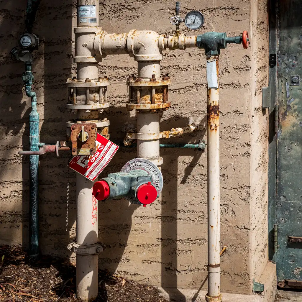 Fire-protection piping with pressure gauges, valves and a red fire-department connection mounted against an exterior wall.