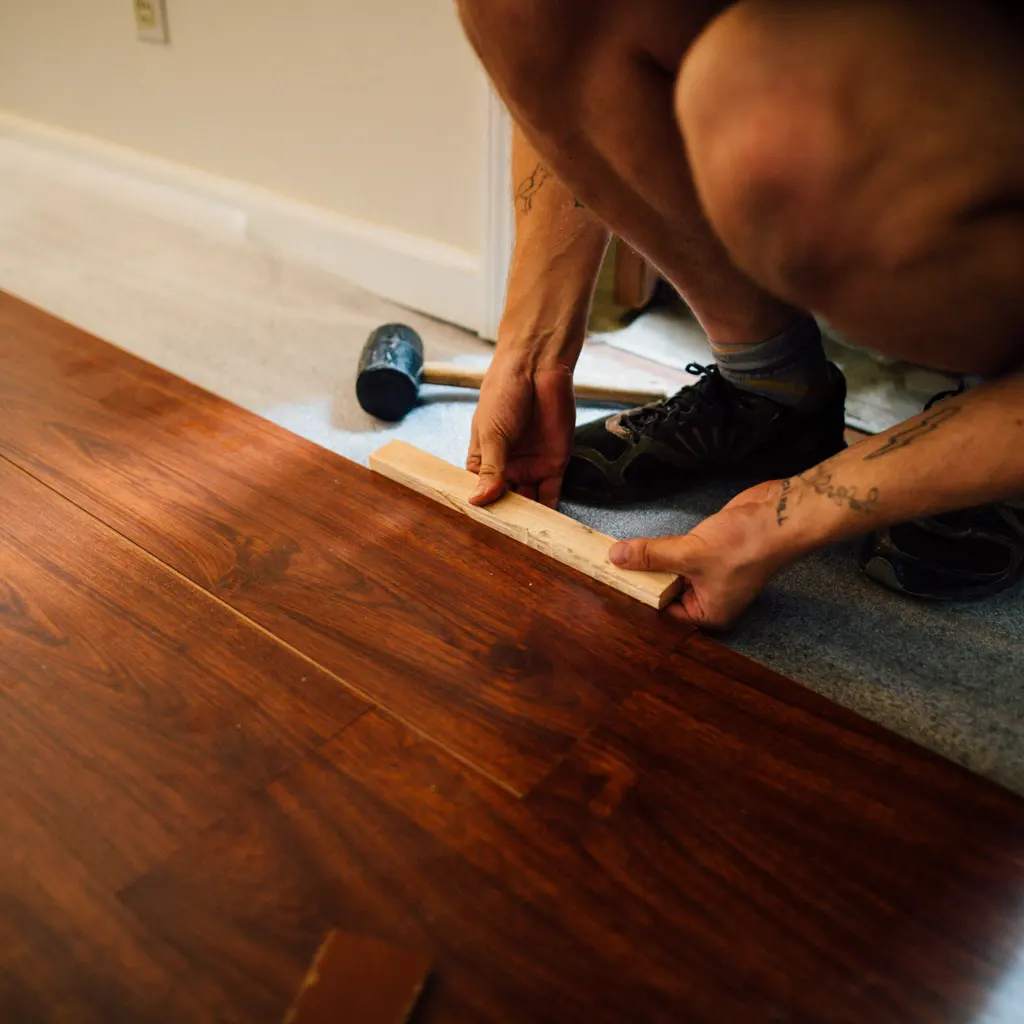 A flooring installer fitting a wood-look laminate plank beside a rubber mallet during an indoor floor-covering project.