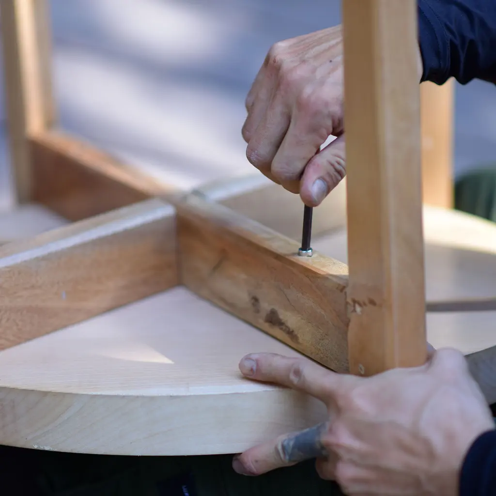 Hands tightening an Allen-key fastener on the underside of a wooden stool during furniture assembly.
