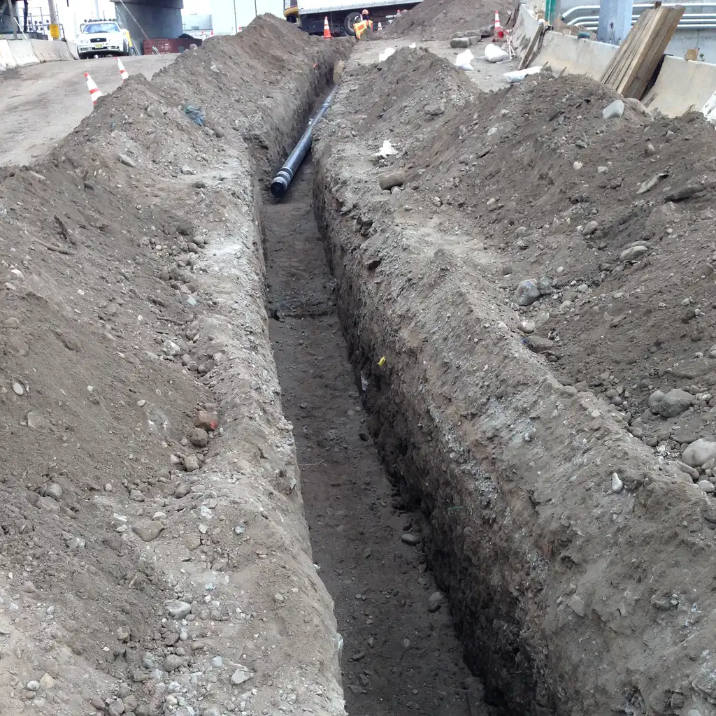 An open utility trench with a pipe section near the far end.
