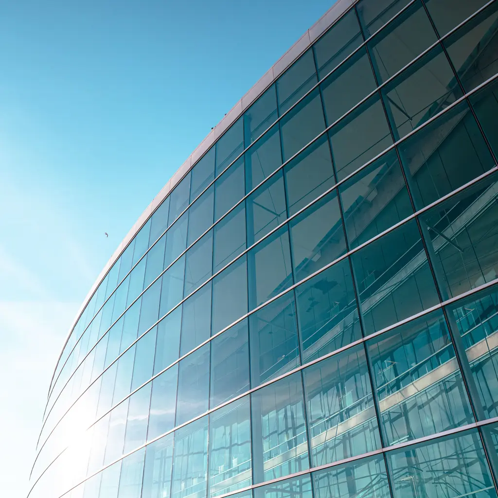 A curved commercial curtain wall with glazed panels and metal mullions reflecting the sky.