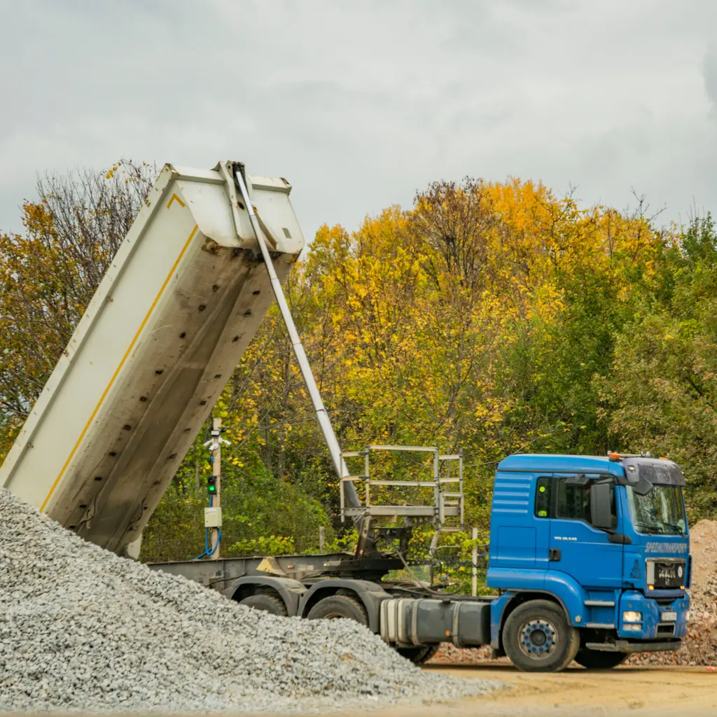 A blue dump truck tipping a load beside a pile of crushed gravel.