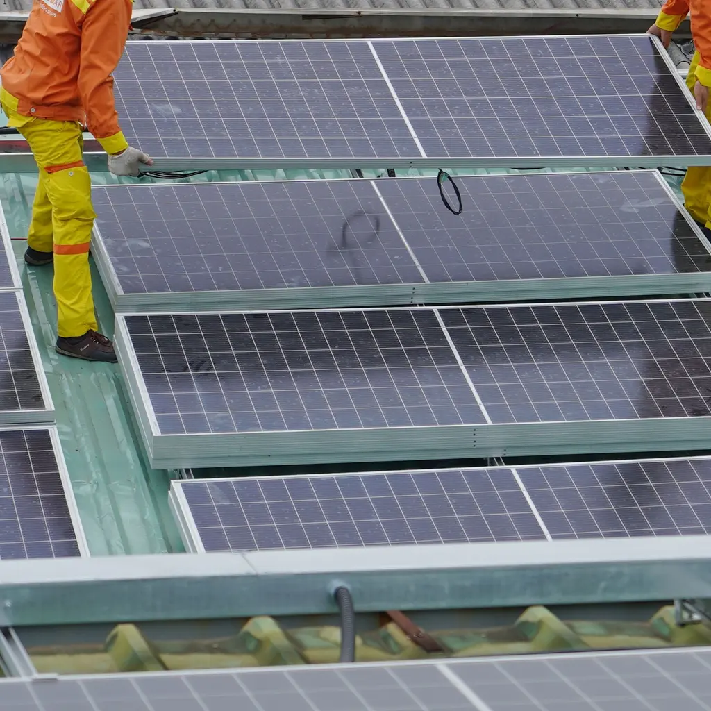 Solar modules being positioned on rooftop rails, with installers’ gloved hands and lower bodies beside the panels.