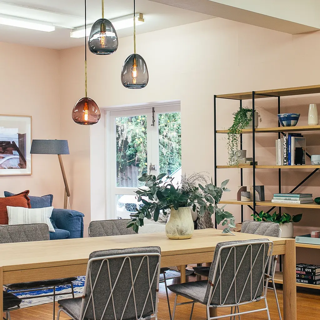 A coordinated living space with pendant lights, wood furniture, shelving, plants and layered neutral furnishings.