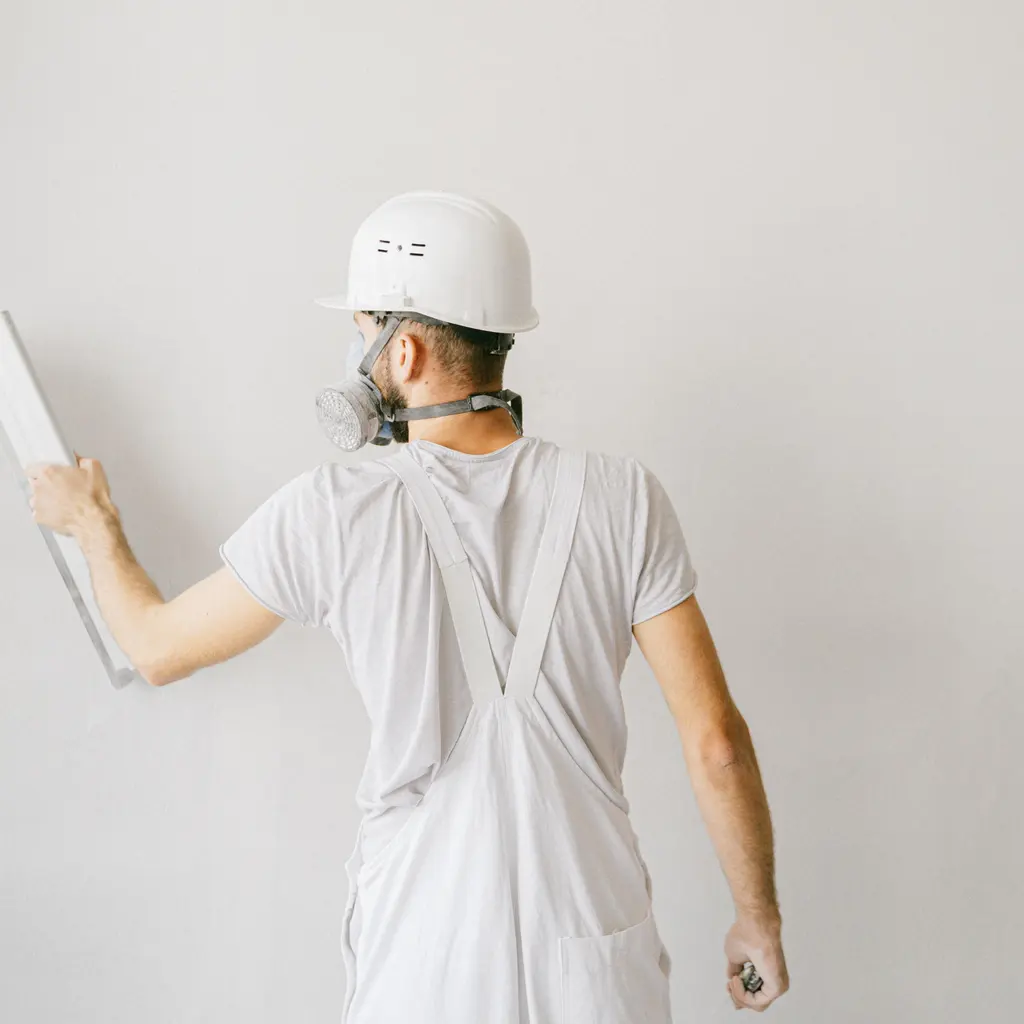Rear view of an interior worker smoothing a white wall with a long finishing tool.