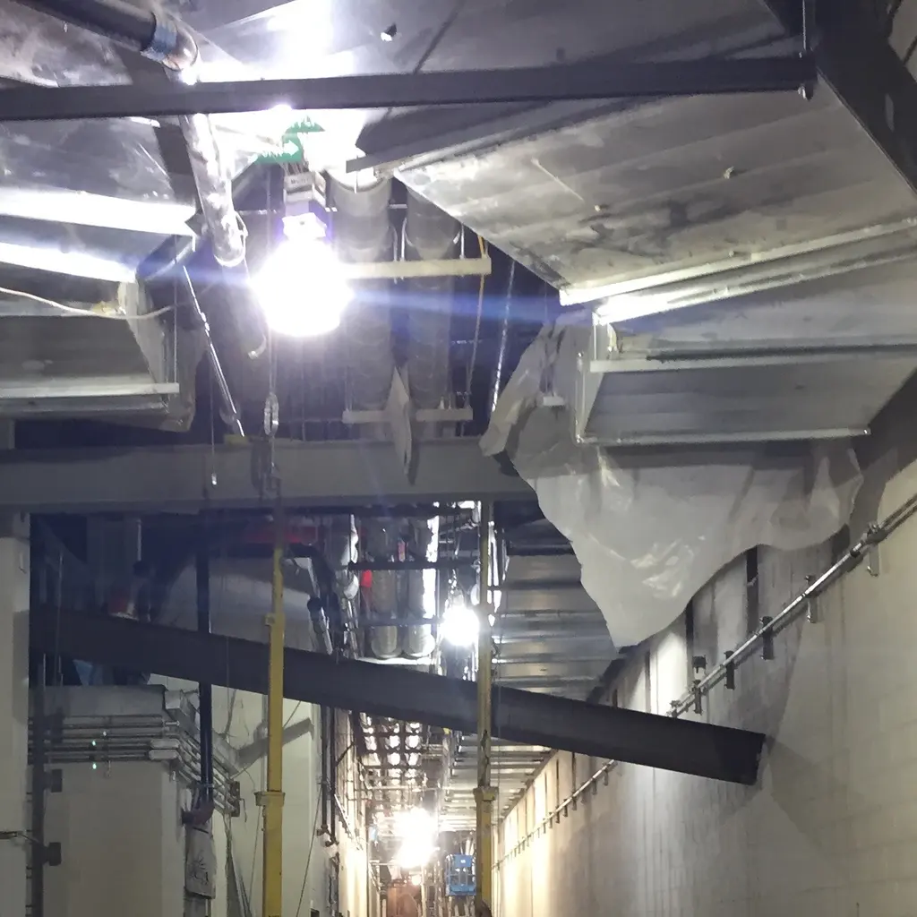 A structural steel beam suspended from rigging inside an unfinished building corridor.
