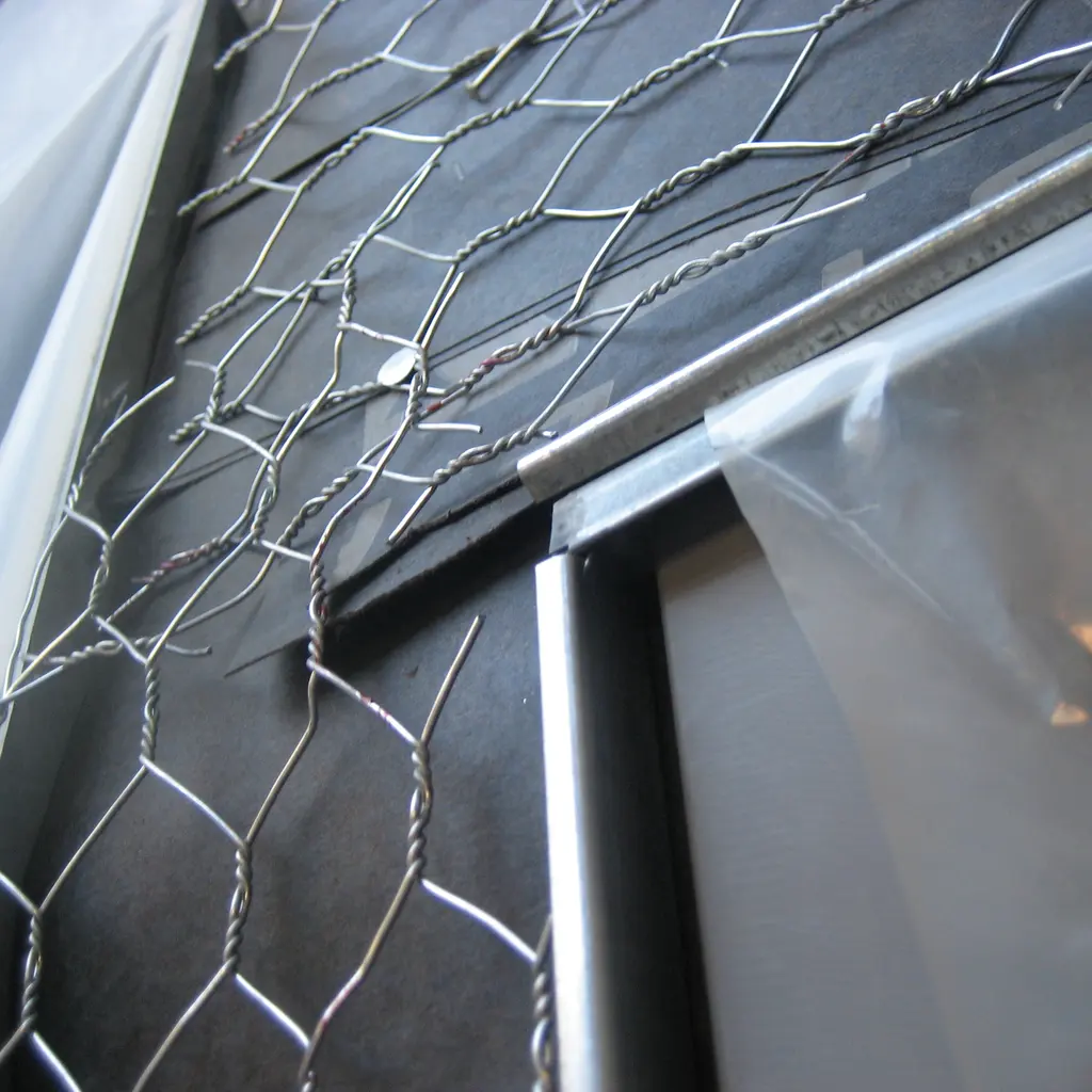Wire stucco lath fastened across building backing beside a framed opening.