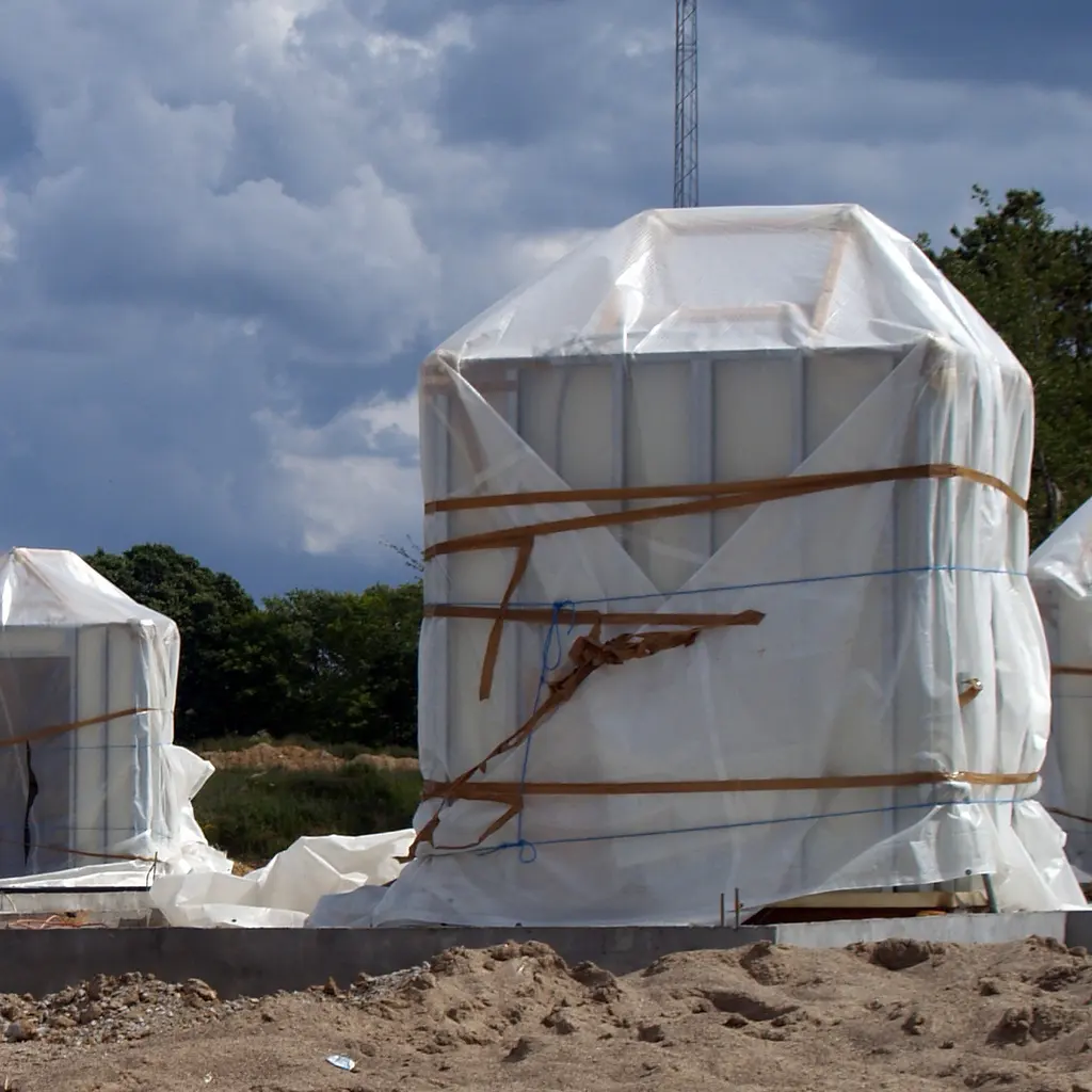 Factory-made bathroom modules wrapped for protection and staged on a building construction site.