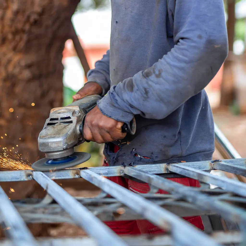 Hands using an angle grinder on a metal framework at the cutting point.