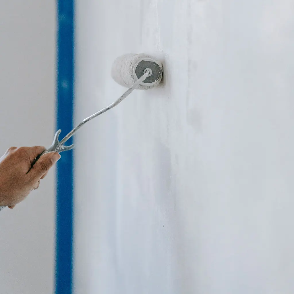 A hand using a small paint roller to apply white paint to an interior wall.