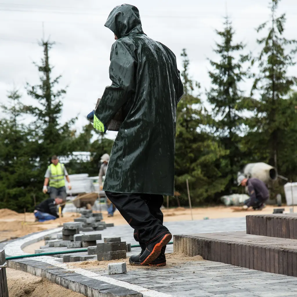 Hooded worker on newly laid paving stones at an outdoor construction site.