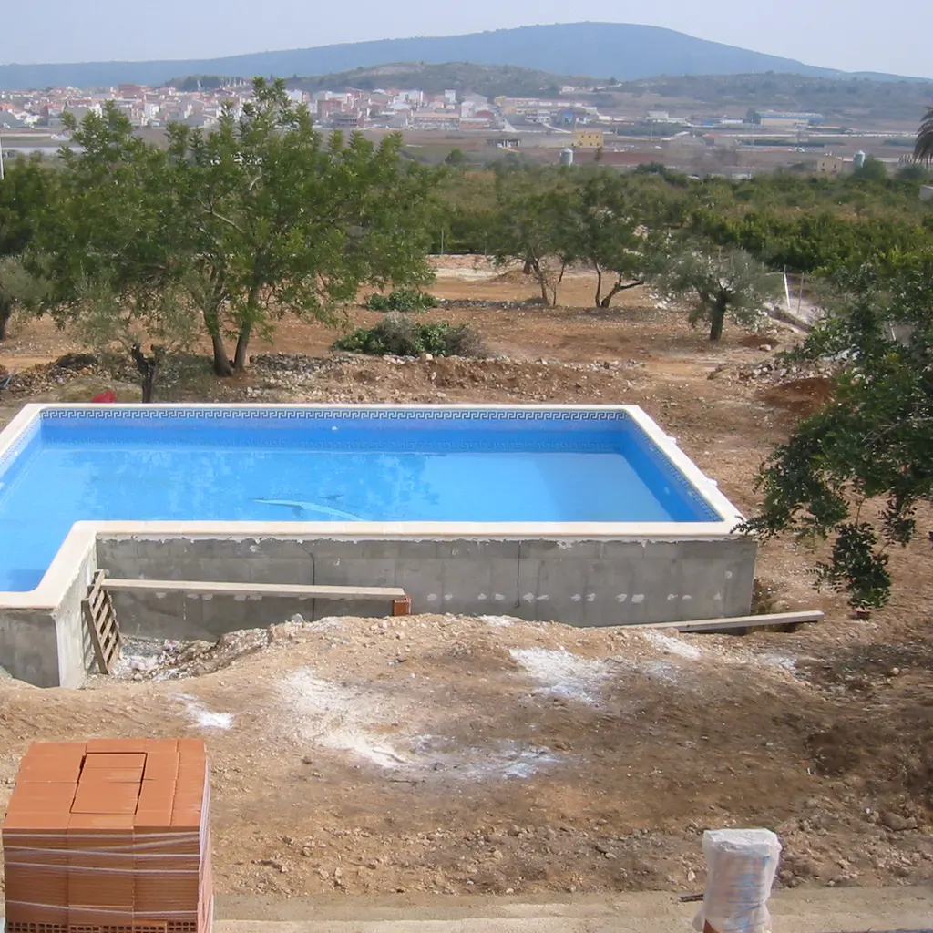 Concrete swimming pool at an unfinished construction site, with exposed outer walls and building materials nearby.