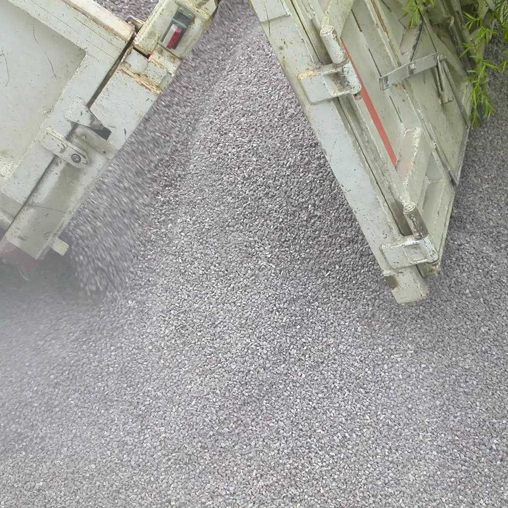 Raised dump-truck bed unloads crushed gravel onto a delivery site.