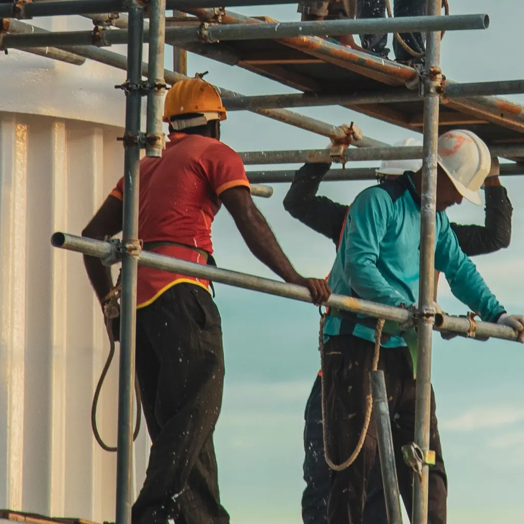 Construction crew assembles tubular scaffold sections beside a building facade.
