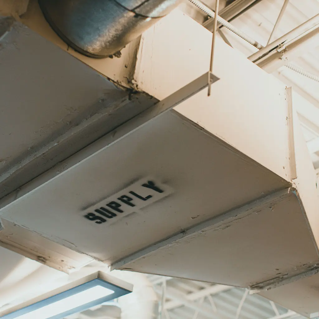 Fabricated rectangular sheet-metal supply duct joins a round branch near an industrial ceiling.