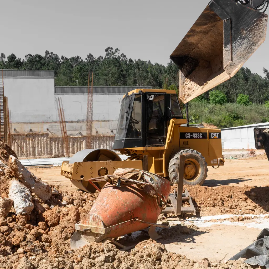 Heavy earthmoving equipment works across excavated soil at a building site.