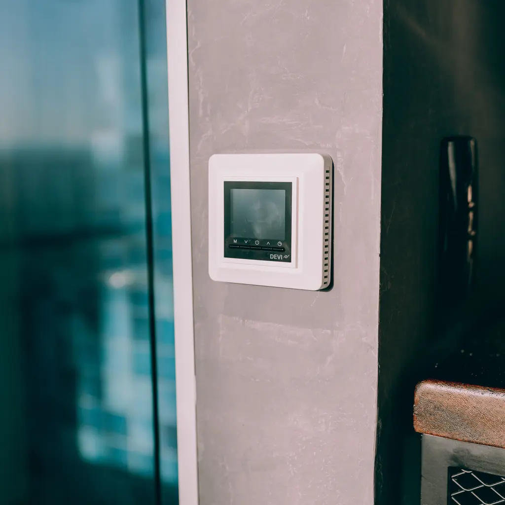 Wall-mounted digital climate controller sits beside a modern interior doorway.