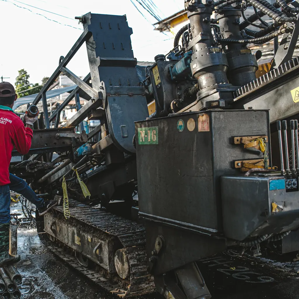 Horizontal drilling machine and stacked drill rods occupy a roadside utility work site.