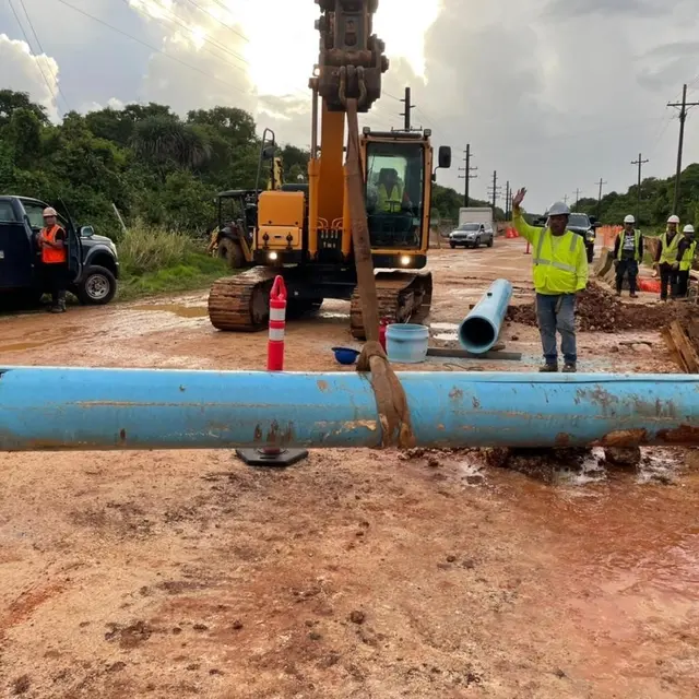 Large blue water-main pipe lies beside an excavator during a roadside supply-line repair.