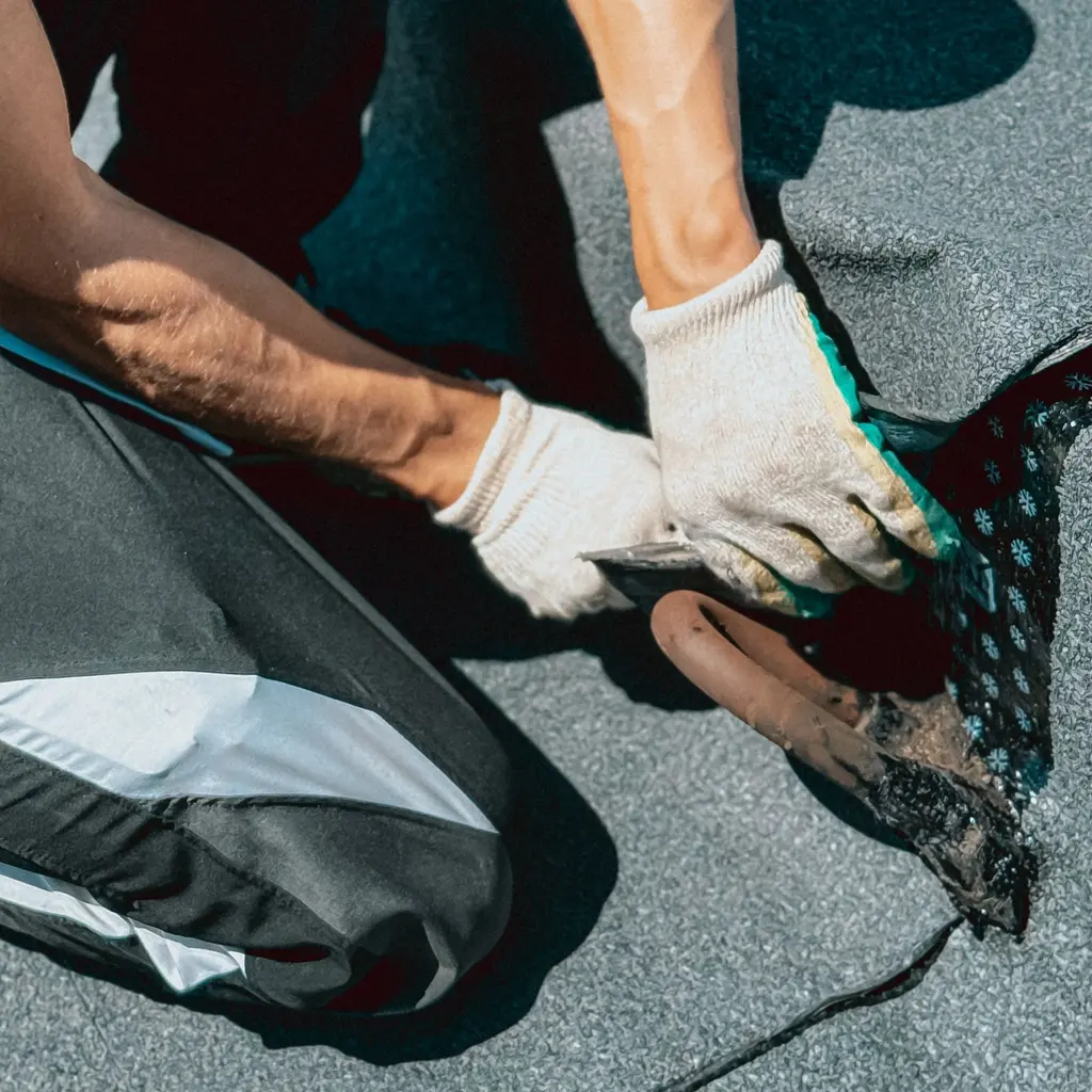 Gloved hands shape a black waterproof membrane at the edge of a flat roof.