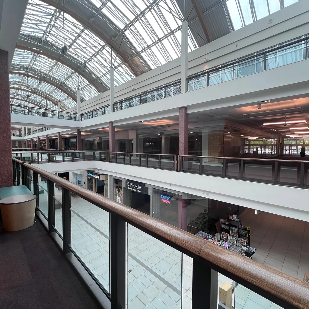 Multi-level shopping mall atrium with glass skylights, open walkways and railings.