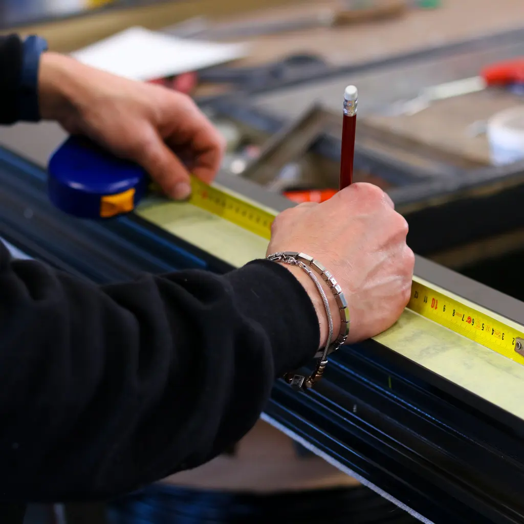 Hands measuring and marking an anodized aluminum profile on a workshop bench.