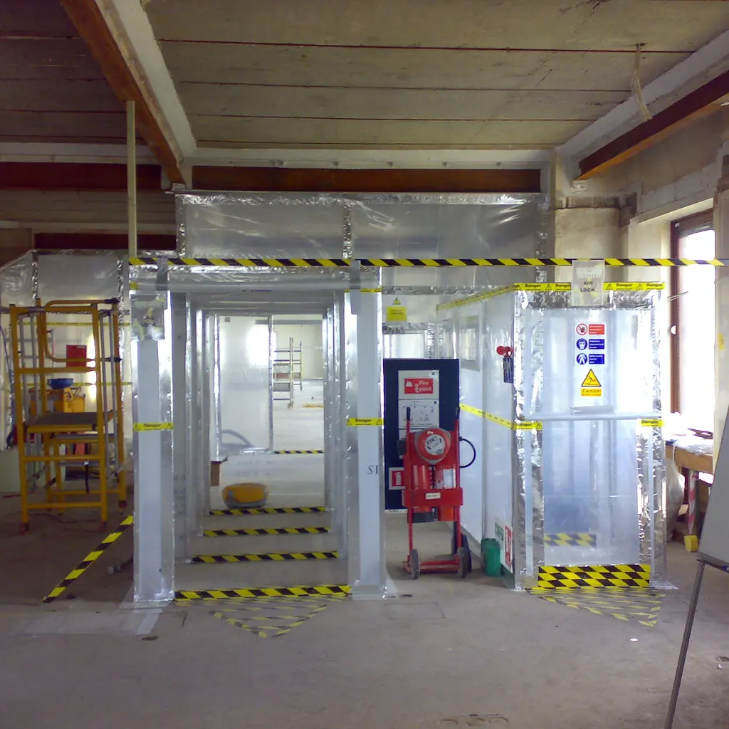 A clear-sheet asbestos-removal containment enclosure with sealed entrances and warning signs.