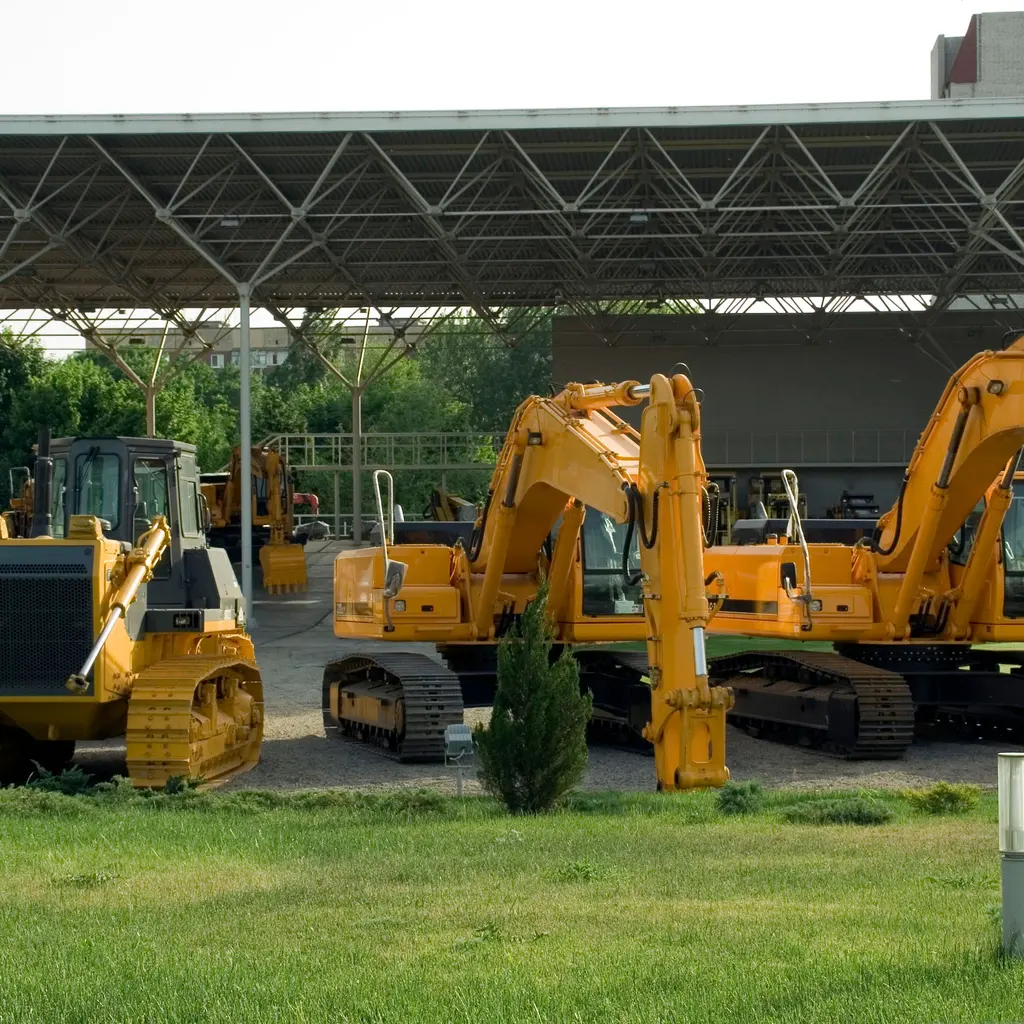 Excavators and a tracked bulldozer staged in an equipment yard under a canopy.
