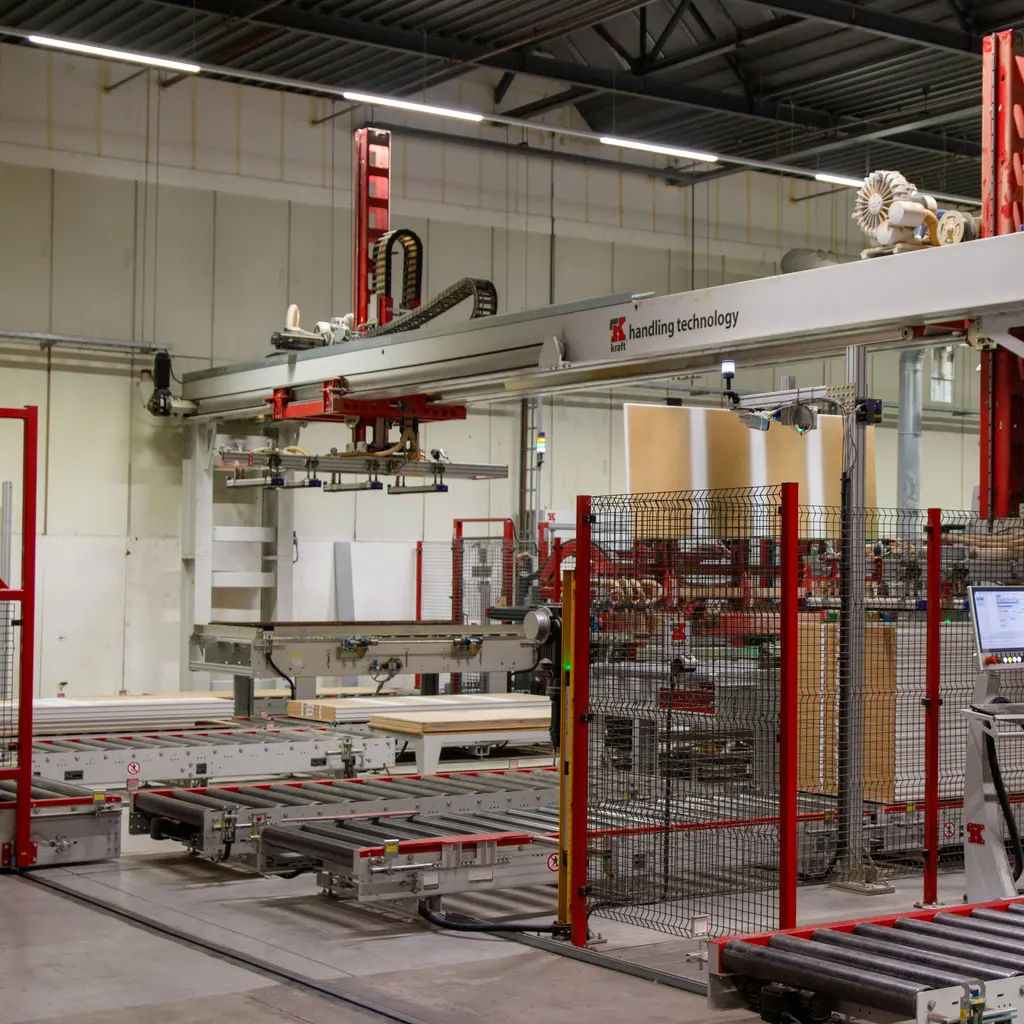 Roller conveyors feeding wooden panels through an automated handling system inside a factory.