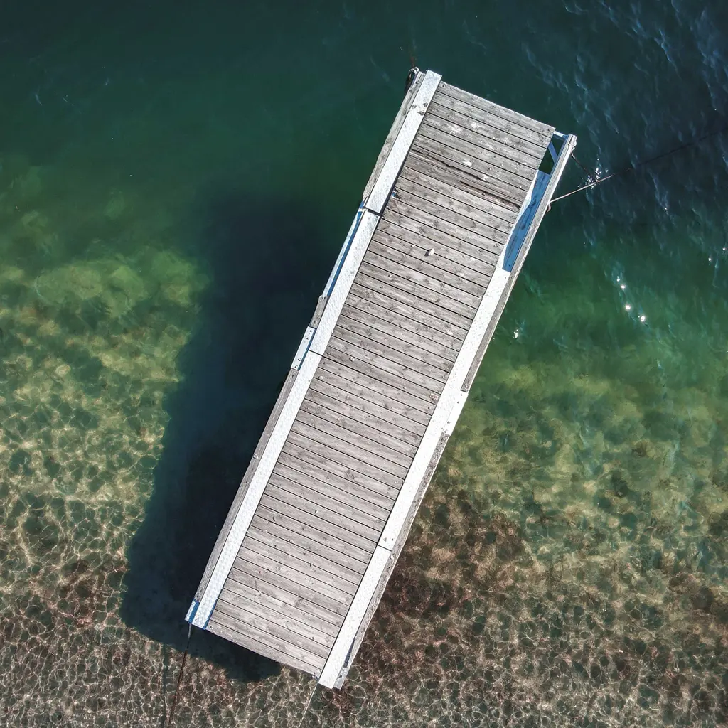 Overhead view of a wooden floating dock extending into clear green water.