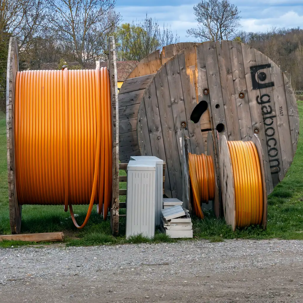 Large reels of orange electrical conduit or cable stock arranged outdoors beside smaller spools.