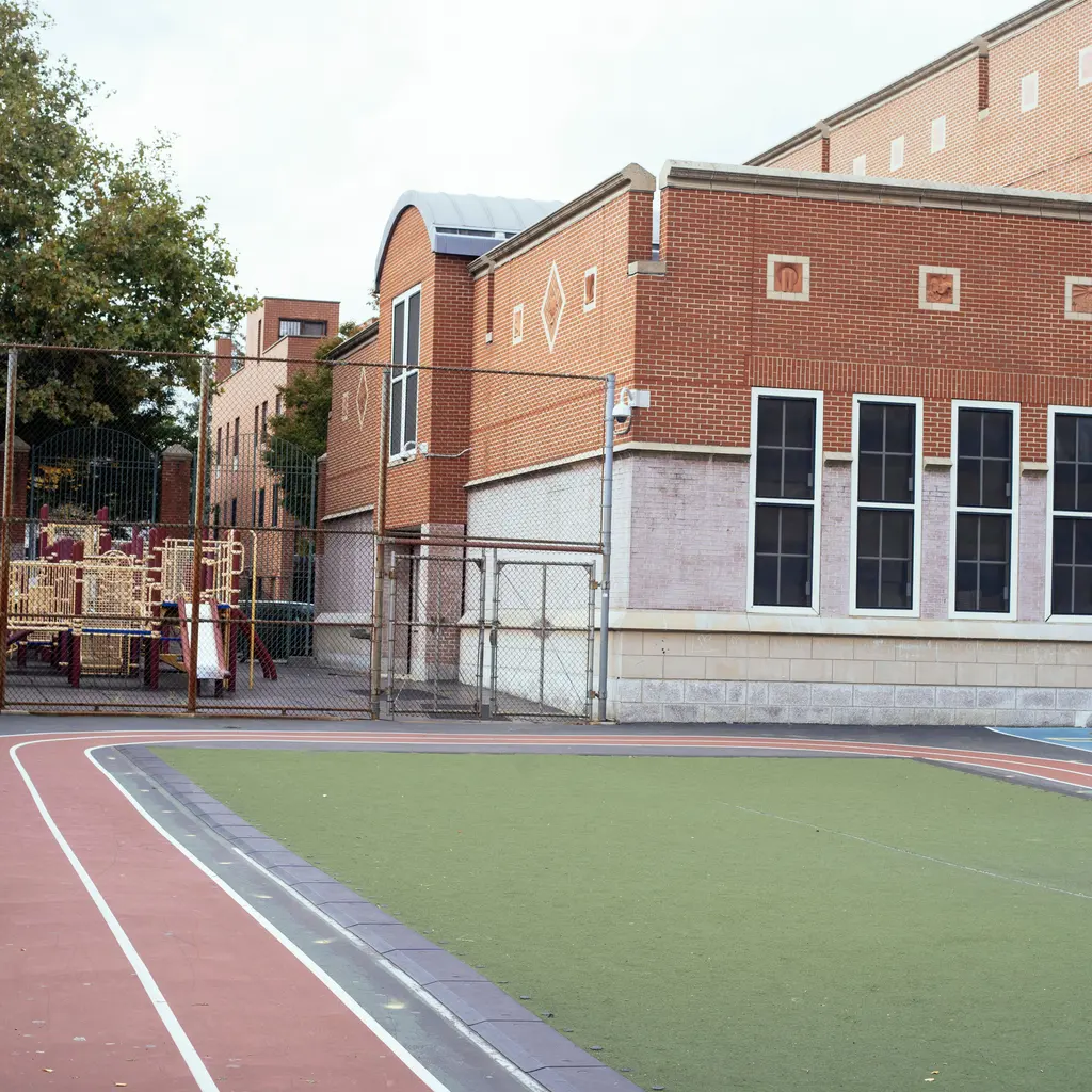 A red-brick school building beside an empty playground and running track.