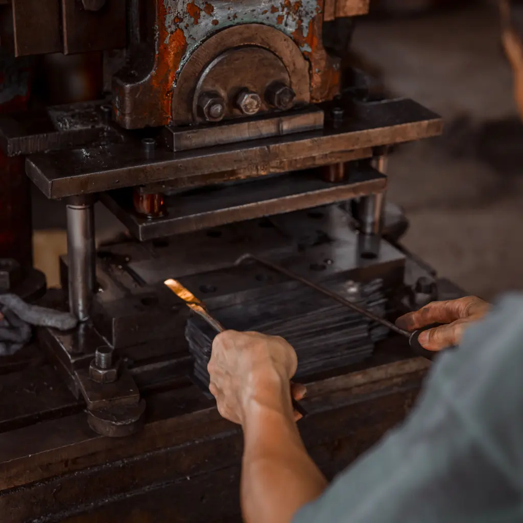 A worker feeding sheet-metal pieces beneath the platen of an industrial press.