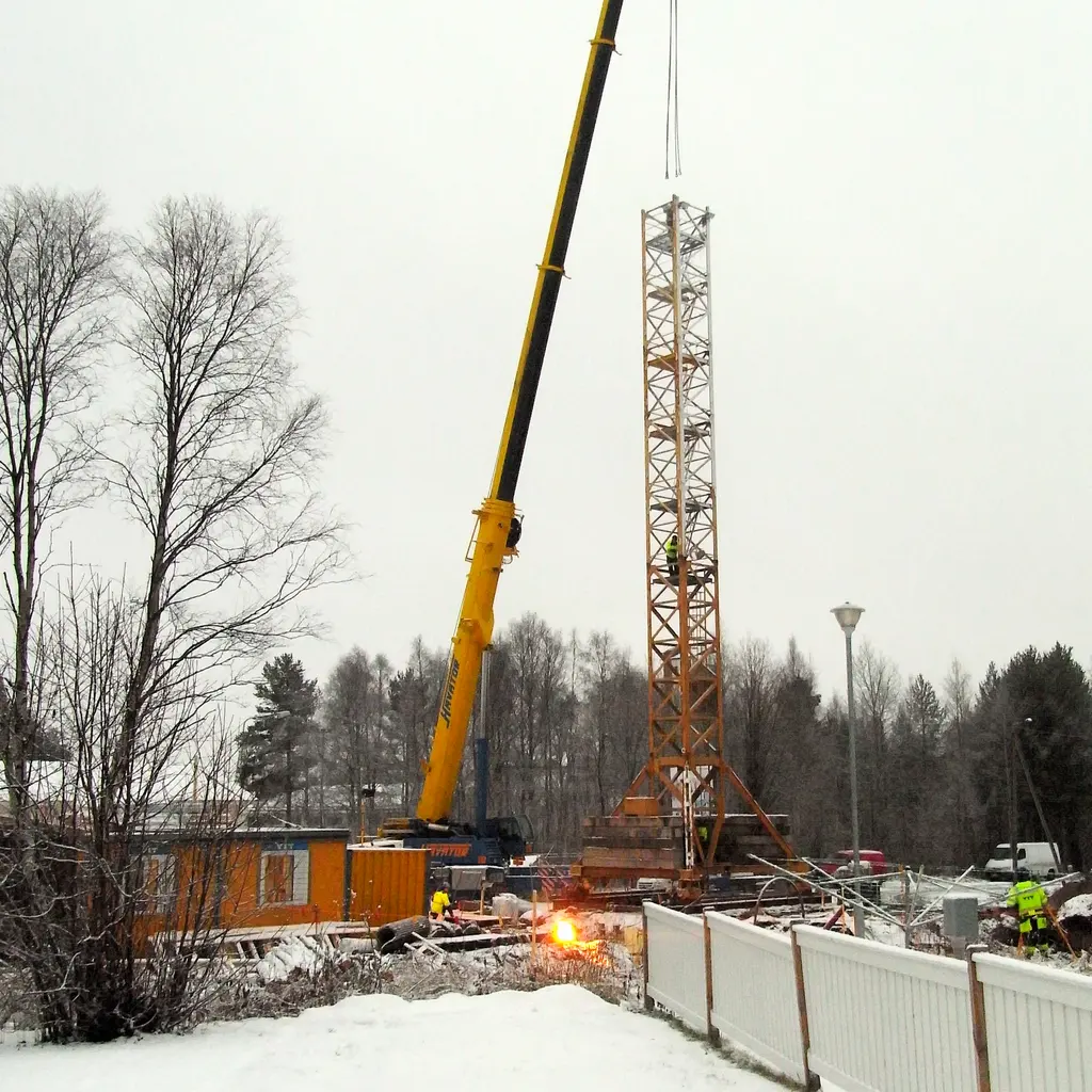 A mobile crane lifting a suspended tower-crane section at a construction site.