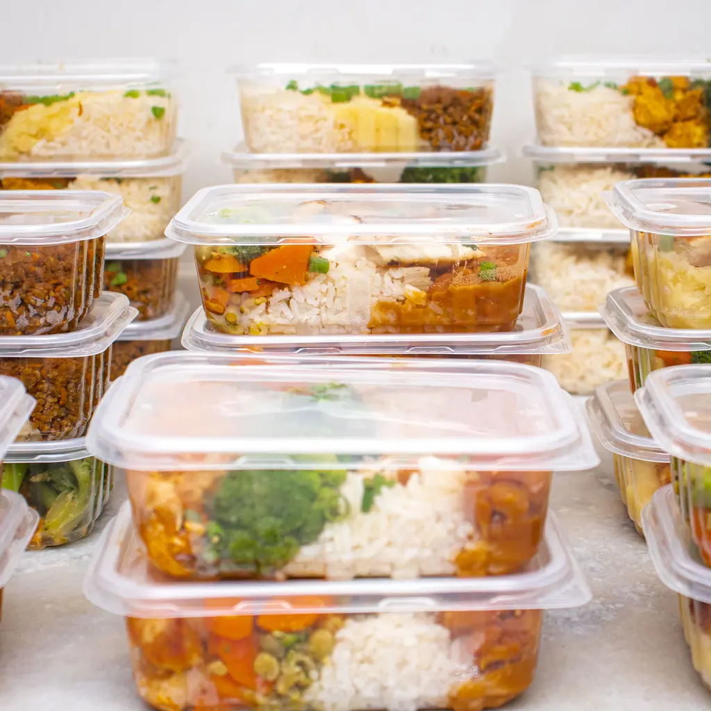 Stacks of clear containers holding prepared meals with rice, vegetables and cooked fillings.