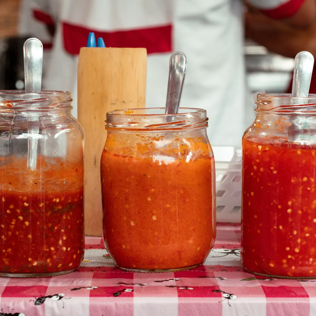 Three open glass jars of red and orange chili sauces, each with a serving spoon.