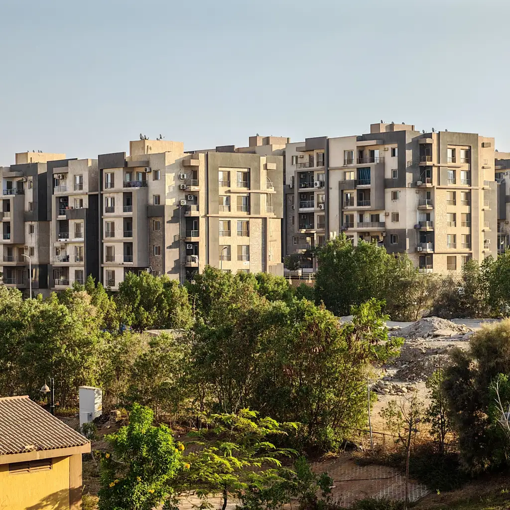 A multi-building apartment complex rising behind trees and landscaped grounds.