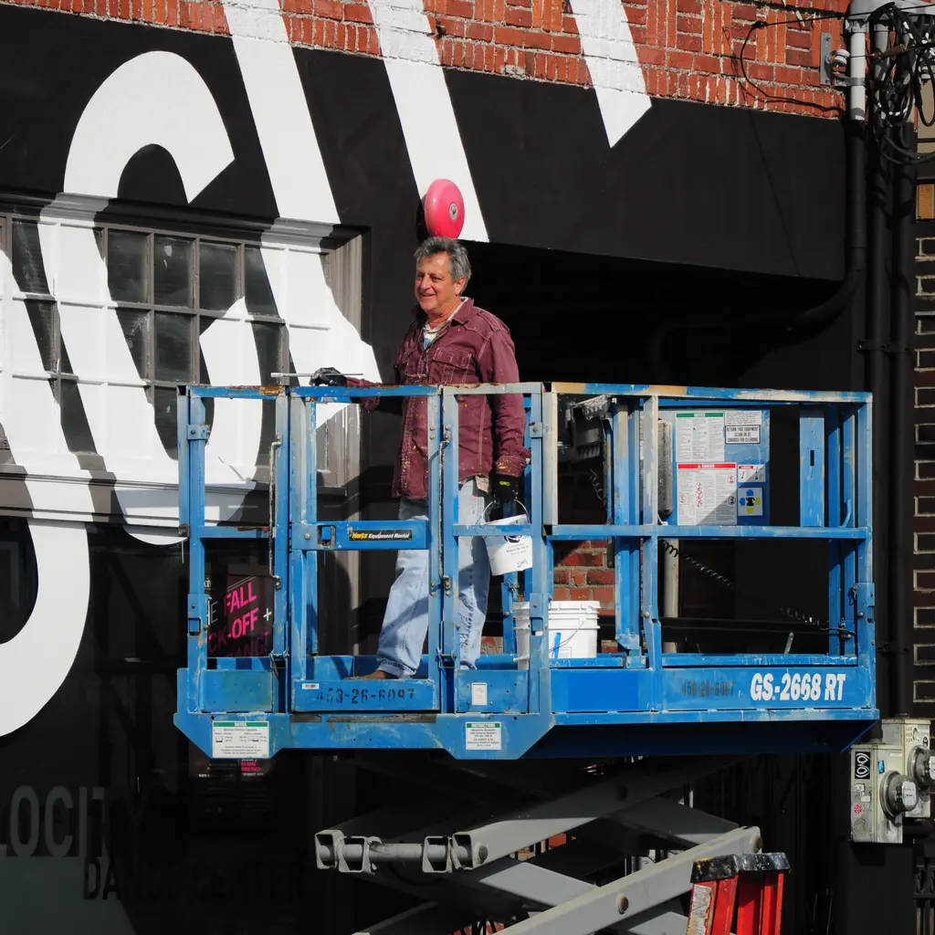 A sign painter on a raised work platform beside large painted letters on a building facade.