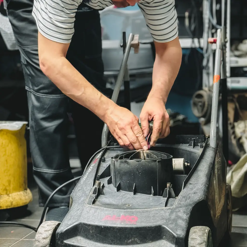 A worker reconnecting wiring in a disassembled lawn mower.
